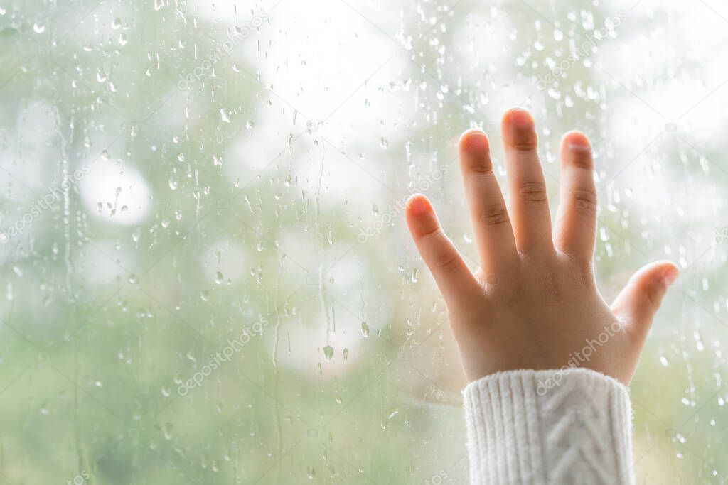 partial view of kid touching window glass with raindrops