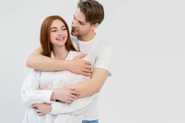 Beyaz tişörtlü, gülümseyen kız arkadaşı kucaklayan adam. 