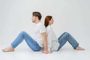Beyaz arka planda sırt sırta oturan genç çiftin yan görüntüsü