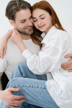 Gülümseyen adam kot pantolon ve gömlek giyen kız arkadaşına sarılıyor. 
