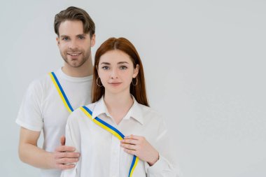 Mavi ve sarı kurdele tutan genç bir kadın. Yanında gülümseyen bir erkek arkadaş. 