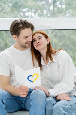 Elinde mavi ve sarı kalp işareti olan olumlu bir adam var ve evde kız arkadaşına bakıyor.