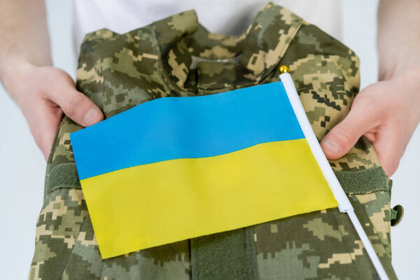 Cropped view of man holding military uniform and ukrainian flag isolated on white 