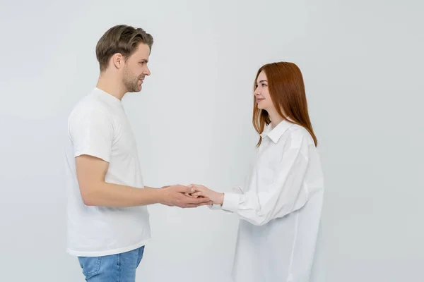 Zijaanzicht Van Jonge Paar Houdend Handen Kijken Elkaar Geïsoleerd Wit — Stockfoto