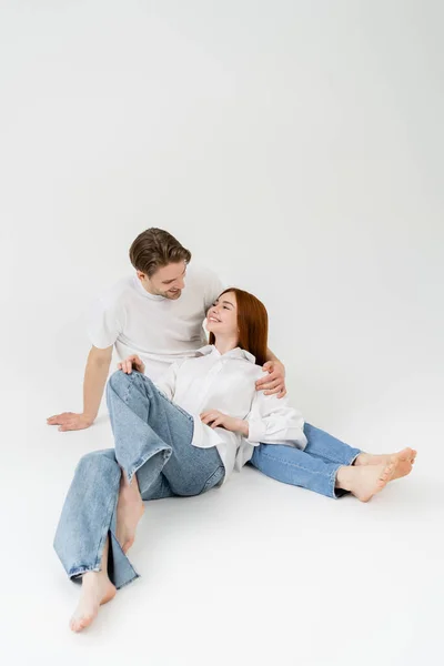 Pareja Sonriente Descalza Mirándose Mientras Está Sentada Sobre Fondo Blanco — Foto de Stock