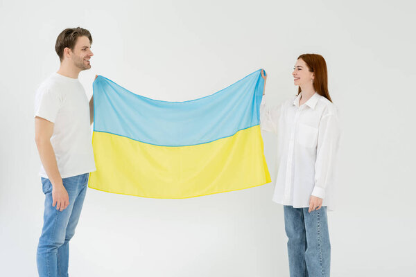 Smiling couple holding ukrainian flag isolated on white 