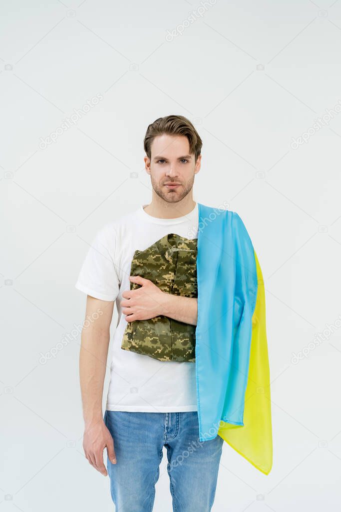 Young man with ukrainian flag holding military uniform isolated on white 