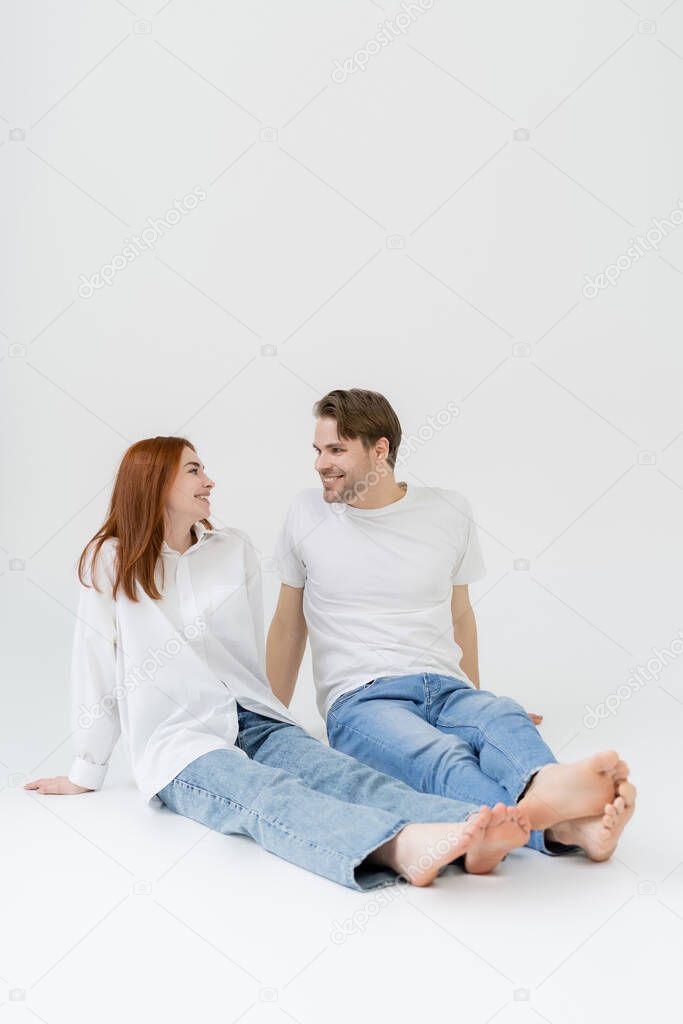 Positive barefoot couple looking at each other on white background