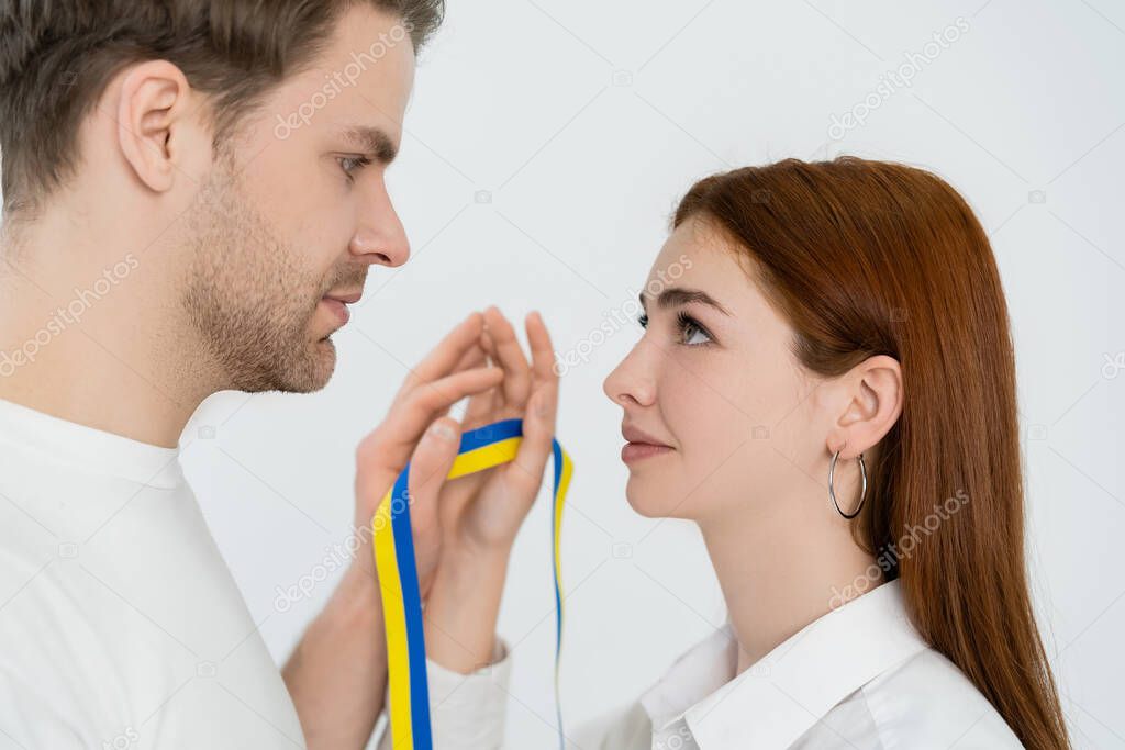 Side view of young couple holding blue and yellow ribbon isolated on white 