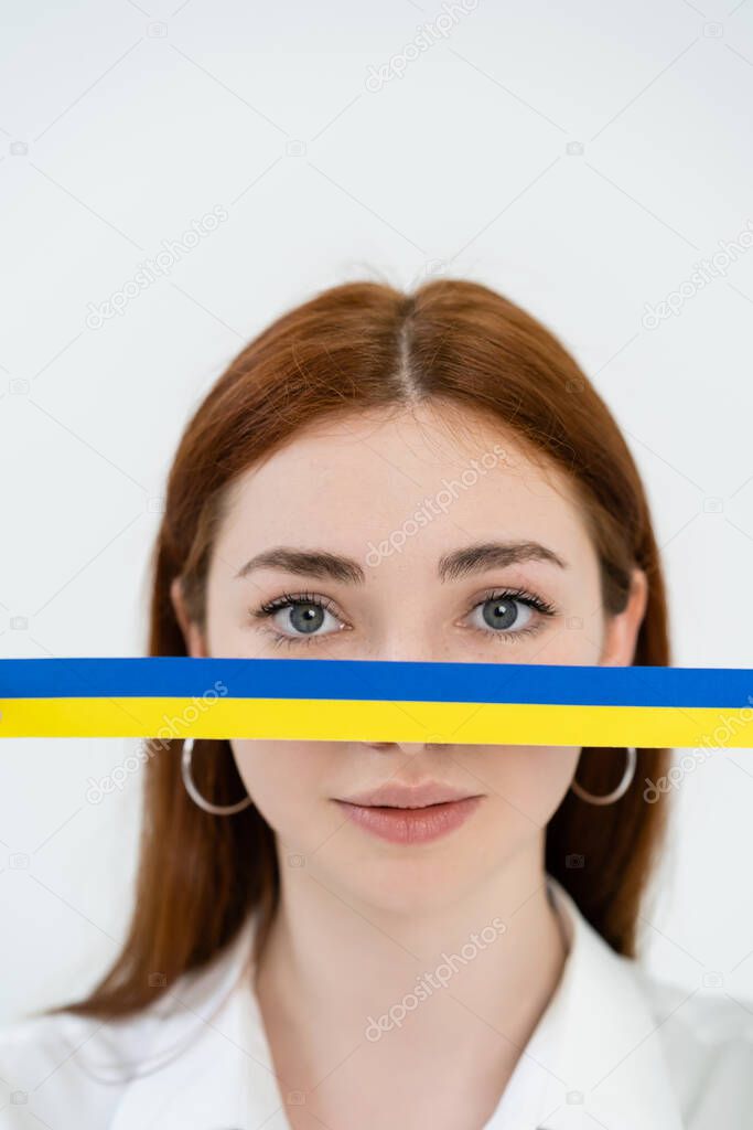 Redhead woman looking at camera near blue and yellow ribbon isolated on white 