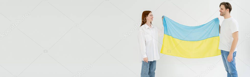 Positive young couple holding ukrainian flag isolated on white, banner 
