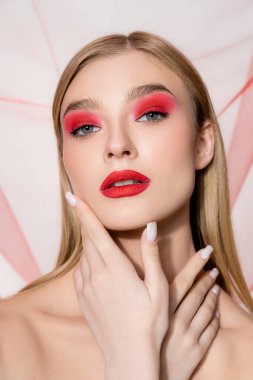 Gri arkaplanda kırmızı göz farı olan açık renk saçlı bir model. 