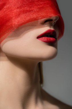 Kırmızı dudaklı ve yüzünde bez olan kadın, gri renkte yalnız poz veriyor. 