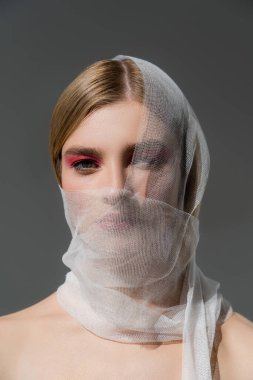 Young woman with naked shoulders and medical bandage on face looking at camera isolated on grey  clipart