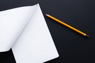 top view of blank notebook and pencil on black