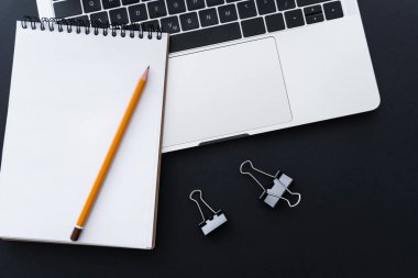 top view of fold back clips near pencil on notebook and laptop on black 