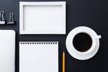 flat lay of fold back clips near notebook, frame and cup of coffee on black 