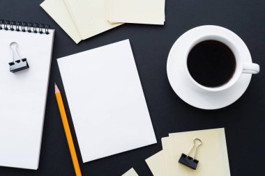 Boş kağıt, defter, kalem, ataçlar ve siyah kahve fincanının üst görünümü