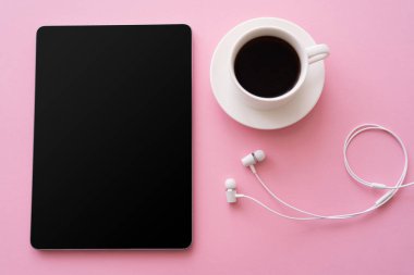 Kahve fincanının yanında boş ekran ve pembe kulaklıklı dijital tabletin üst görüntüsü 