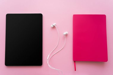 Kulaklıkların yanında boş ekran ve pembe üzerine parlak not defteri olan dijital tabletin üst görünümü