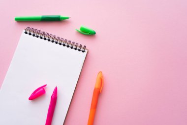 top view of colorful pens near blank notebook on pink