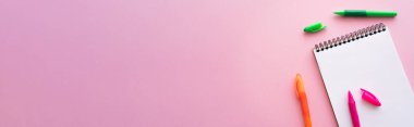 Pembe, afiş üzerine boş defterin yanındaki renkli ve parlak kalemlerin üst görünümü