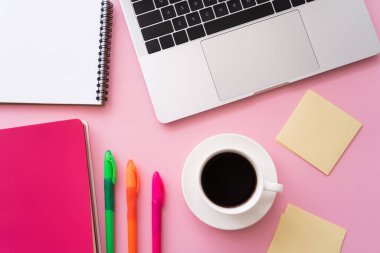 Kırtasiyenin yanındaki dizüstü bilgisayarın üst görüntüsü ve pembe üzerine bir fincan kahve. 