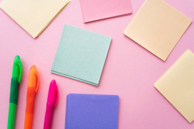 top view of colorful pens near blank paper notes on pink