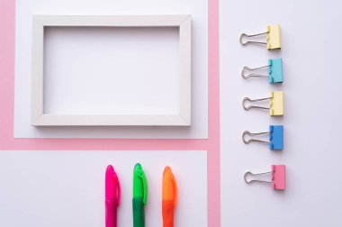 Boş çerçeve ve pembe kağıtların yanındaki renkli kırtasiyenin üst görünümü