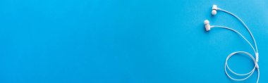 top view of white wired earphones on blue, banner