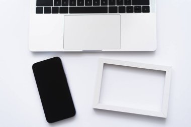 top view of smartphone near laptop and frame on white