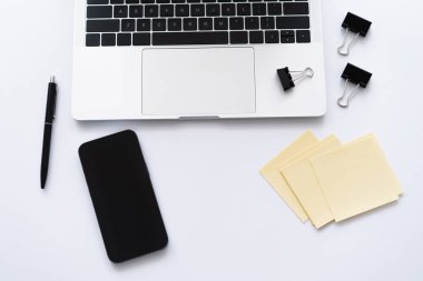 Bilgisayarın yanındaki akıllı telefonun üst görüntüsü ve beyaz üzerine kırtasiye.