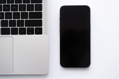 Beyaz dizüstü bilgisayarın yanında boş ekranlı akıllı telefonun üst görünümü