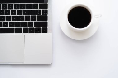 top view of cup of coffee near laptop on white