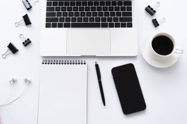 top view of smartphone with blank screen near laptop, earphones and stationery on white