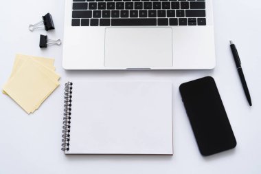 top view of smartphone with blank screen near laptop and stationery on white