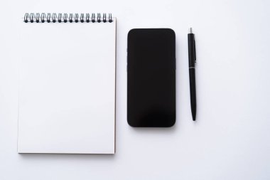 top view of mobile phone with blank screen near notebook and pen on white