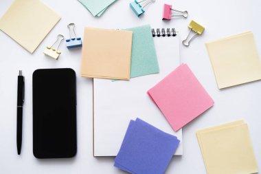 top view of smartphone with blank screen near pen and stationery on white