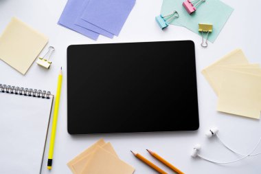 Boş ekranlı dijital tabletin üst görünümü ve beyaz sayfanın yanındaki kulaklıklar