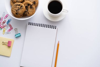 top view of cup of coffee, cookies and stationery near smartphone with blank screen on white