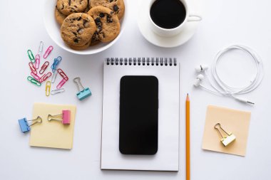 Kahvenin, kurabiyelerin ve akıllı telefonun beyaz kırtasiyenin yanındaki boş ekranın üst görüntüsü.