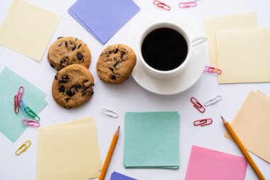 top view of chocolate chip cookies and cup of coffee near stationery on white