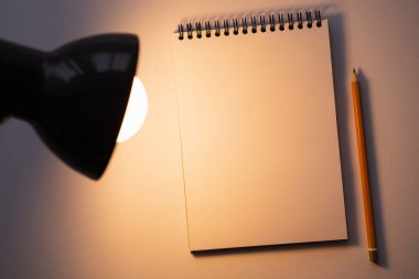 top view of blank notebook near pencil and turned on lamp on white clipart