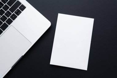 top view of blank paper near laptop on black 
