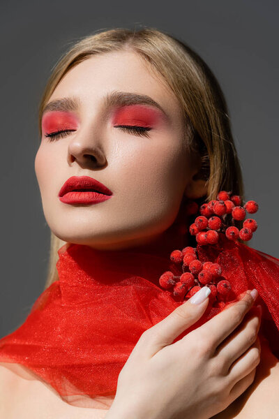 Fair haired model with red makeup touching berries on cloth isolated on grey 