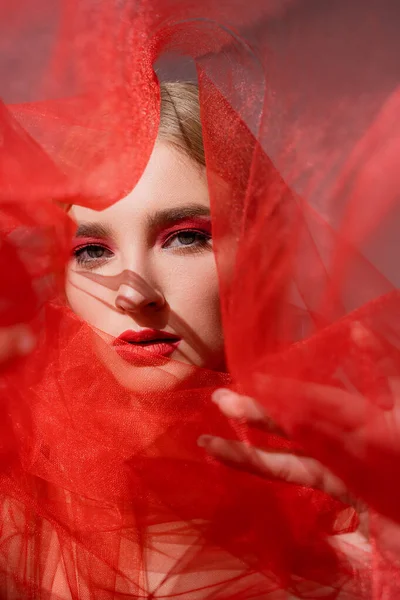 Modelo Joven Con Maquillaje Rojo Mirando Cámara Cerca Tela Borrosa — Foto de Stock