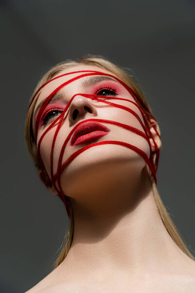 Low angle view of woman with red makeup and threads isolated on grey 