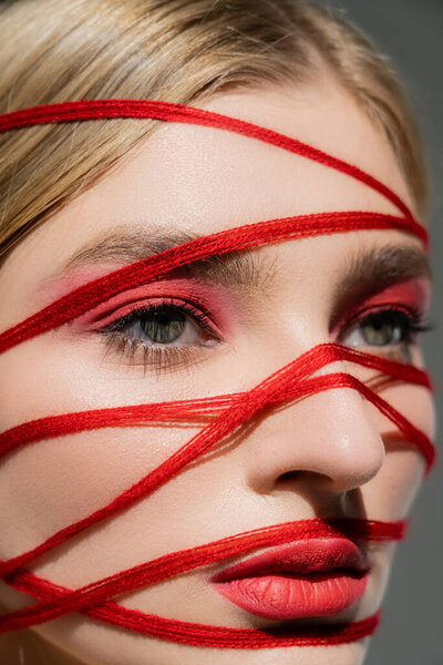 Close up view of red threads on face of woman with makeup isolated on grey 