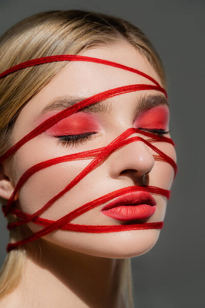 Fair haired woman with red visage and threads on face closing eyes isolated on grey 