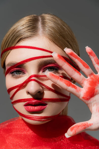 Model with red visage, threads and paint on hand isolated on grey 